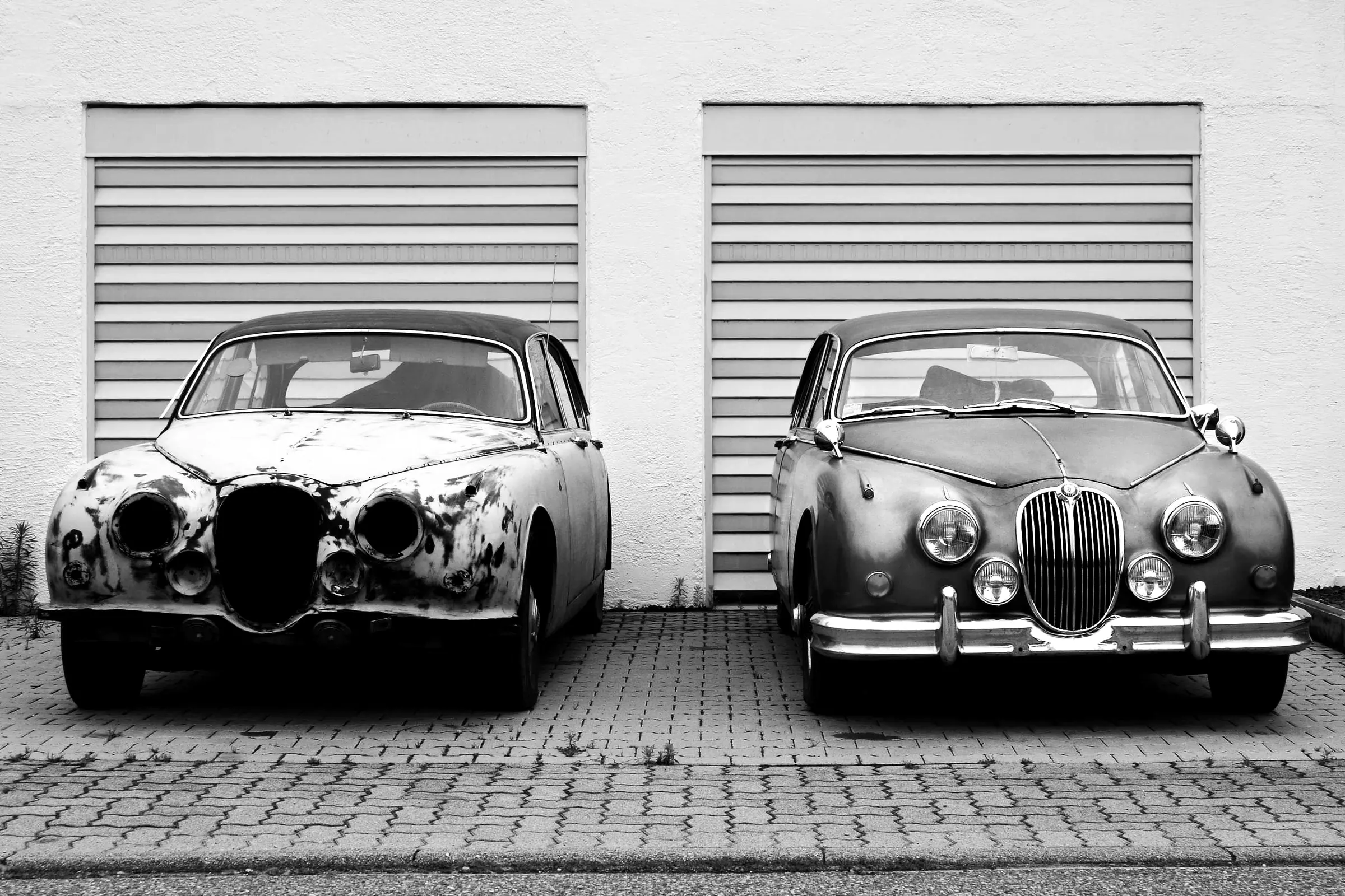 Two old cars parked in front of shuttered garages