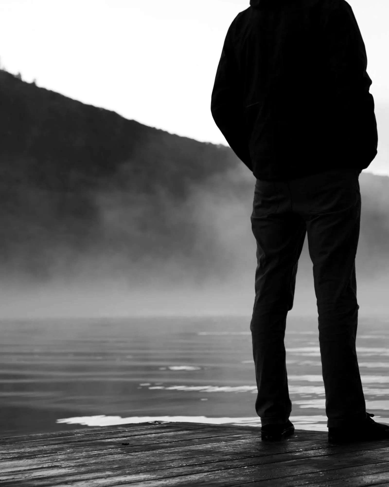 A man in dark clothes at a misty lake edge
