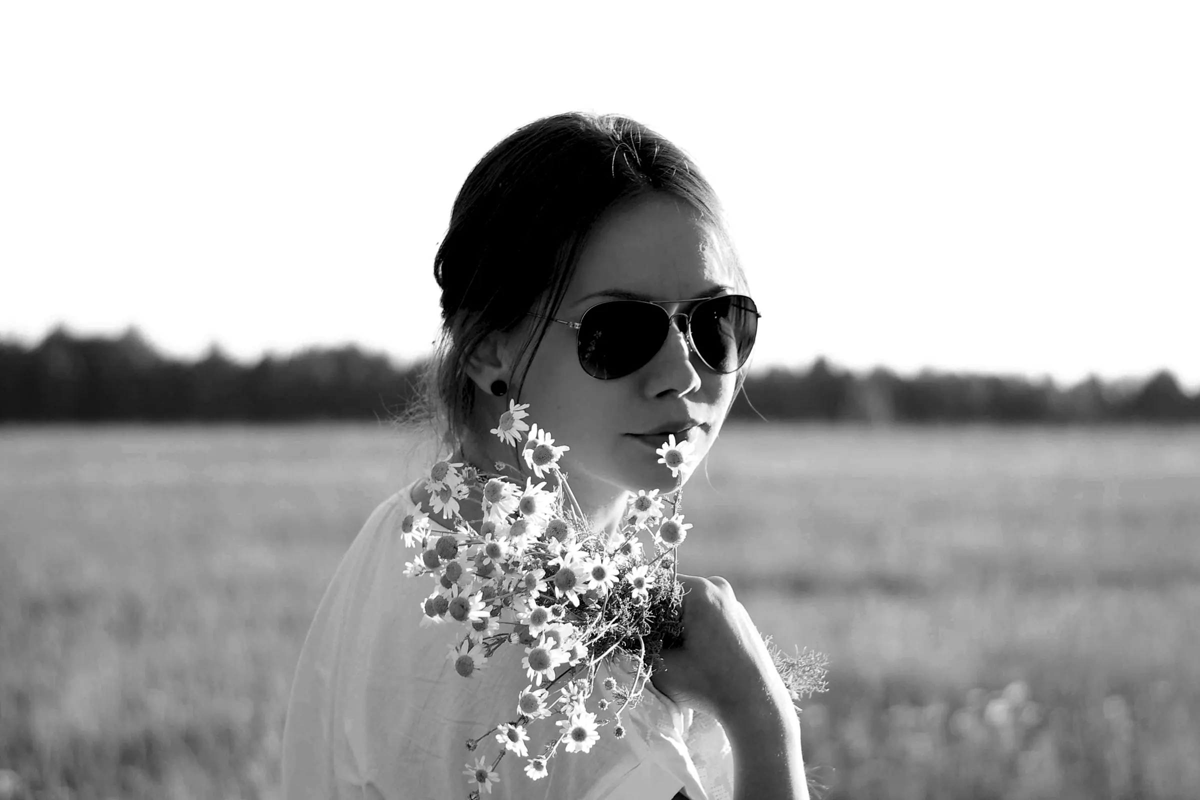 A woman in sunglasses in a field, flowers at her chest