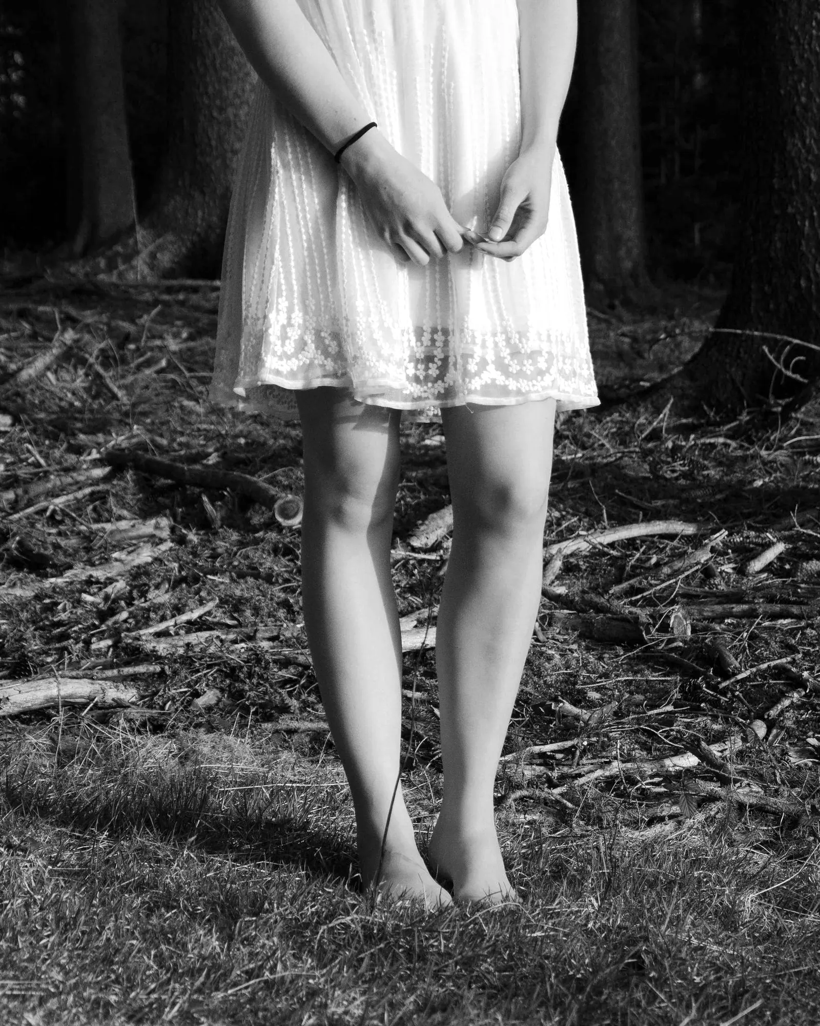A girl in a light dress, hands clasped, in a wood
